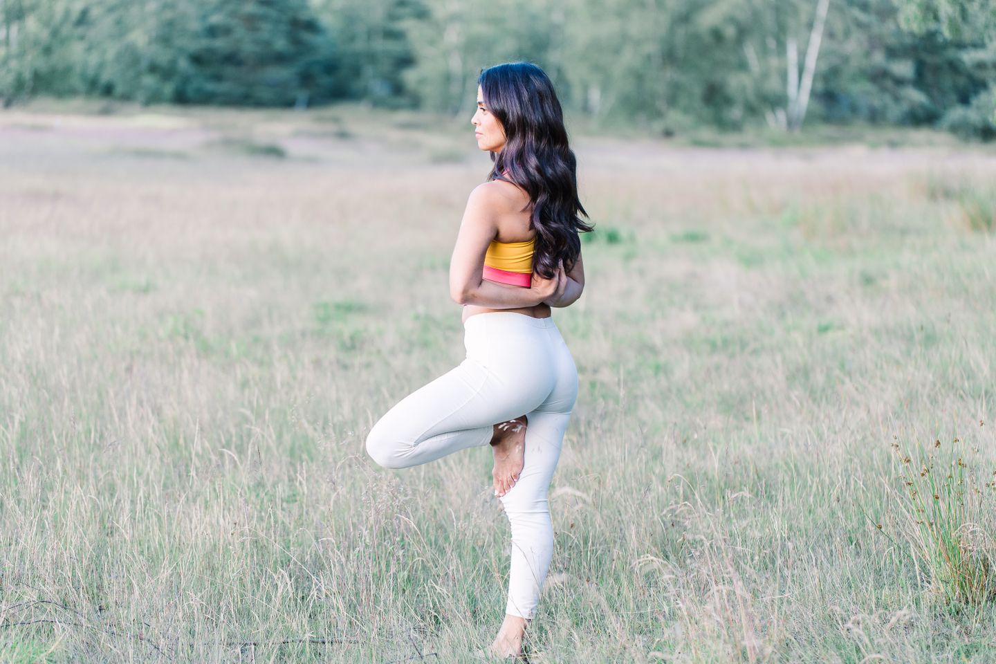 Side view of a woman balancing in a yoga pose outdoors on a grassy field, promoting wellness and fitness.